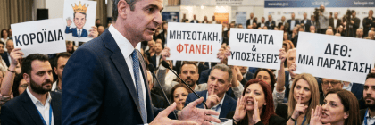 Greek political speaker at HELEXPO surrounded by attendees holding protest signs